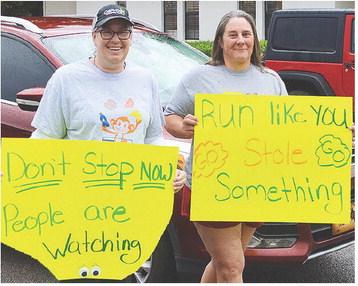 Danielle Helch, left, and Tina Reinschmiedt show off their creative signs they used to encourage runners during the races. CDN | Micah Ashcraft
