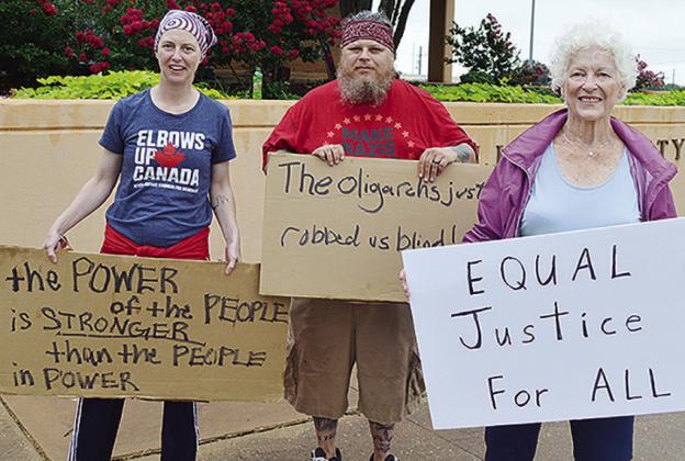 From left, Kyla McMillon, Shawn McMillon, and GeoReta Jones stand Friday in front of Clinton City Hall with signs to participate in the “No Kings” protest. CDN | Micah Ashcraft