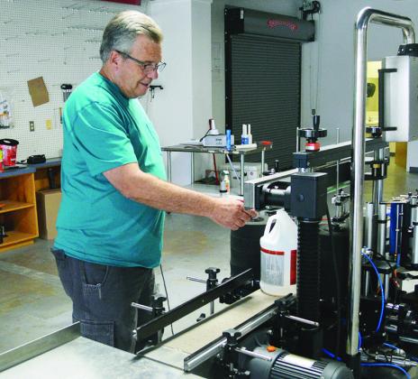Marvin Wesley demonstrates how product containers move through the label machine Wednesday at the future site of Frontier Packaging on the corner of S. 4th Street and Avant Avenue. CDN | Christian Jacobsen