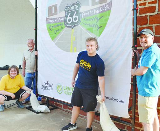 From left, Ethan Baker, Clinton Mayor David Berrong, Cademon Smith, and Steve Weichel setting up one of the backdrop posters on the amphitheater stage.