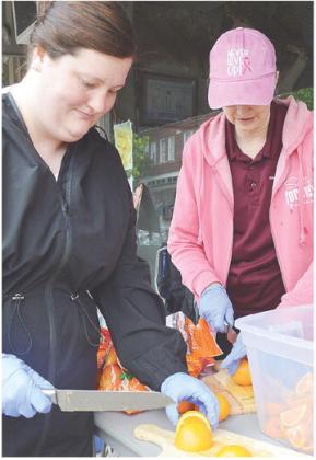 Taylor Hamlin, left, and Brenda Burton cut up orange slices Saturday morning on Frisco Avenue to hand out to runners as they finish their races during the Clinton Classic Run. CDN | Micah Ashcraft