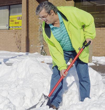 Chan Martin goes in and out of S&amp;D Drug, while using a shovel to clear the sidewalk of snow, in hopes of fighting the cold temperatures Monday morning. CDN | Micah Ashcraft