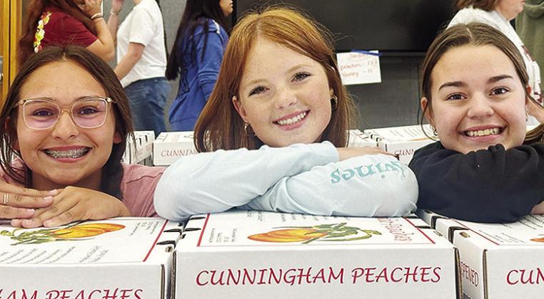 From left, Tatum Fanshier, Bella Bridgeman, and Tatum Shackelford with the Clinton High School Choir stop for a photo as they unload boxes of peaches sold as part of their annual peach sale fundraiser Tuesday afternoon at the high school. CDN | Staff Phot