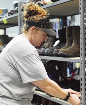 Mickie Haag stocks several pairs of newly donated boots to the “Boot Room” shelves Wednesday morning at the Clinton Mission House Wear It Again store. CDN | Micah Ashcraft