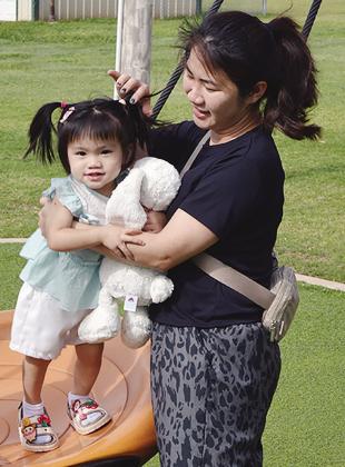 Audrey Nguyen, left, balances on the swing as Anh Dao helps her stand up Wednesday at the McLain Rogers Park Playground. CDN | Christian Jacobsen
