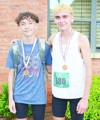 Brothers Bentlee Hernandez, left, and Xadrian Hernandez smile as they show off their gold medals after winning the 5K and 10K races of the recent Clinton Classic Run on Frisco Avenue. CDN | Sam Goodwyn