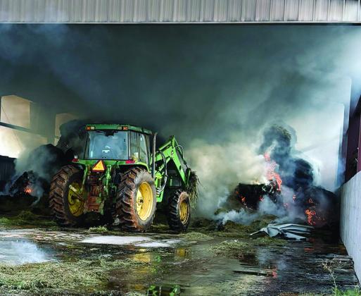 A tractor works to remove hay bale debris Tuesday morning at Tim Davis’ barn located on N. 28th Street The Clinton Fire Department responded to the hay bale barn fire and it is estimated more than 500 bales ignited in the blaze. CDN | Courtesy photo