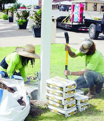 Cameron Jones, left, and Caleb Mabry work on cementing the pole in place Thursday that will hold a new Route 66 centennial sign outside of the Frisco Center. It’s visible on the trailer in the background. CDN | Sam Goodwyn