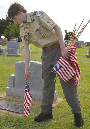 Eagle Scout Owen Lavigne, a member of Troop 361, plants flags in front of headstones at Clinton Cemetery, alongside his fellow scouts as well as members of the American Legion, in preparation for the Memorial Day ceremony set for 10 a.m. Monday. CDN | Mic