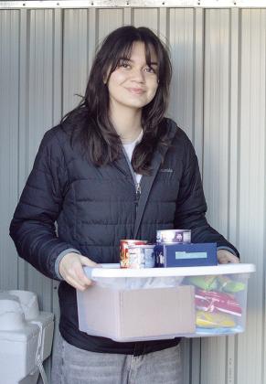 Carys Garcia carries a stack of donated food to the community food box she set up behind the Garcia Law offices Wednesday morning. CDN | Micah Ashcraft