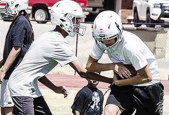 Zaithan Whiteshirt, left, hands the ball off to Camron Lime during the first day of middle school football practice at the high school practice field. CDN | Sam Goodwyn