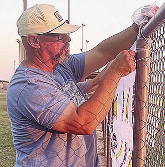 Tournament Director Nathan Meget hangs up signs at Schumacher Fields at Acme Brick Park Tuesday in preparation for the OK Kids 8U State Softball Tournament