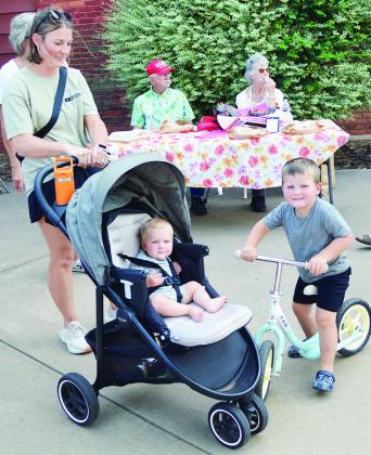 From left, front, Kassy, Bowen, and Barrett Bonham visit the Farmers Market and enjoy the sun Thursday at Engleman Park. In the back, Bill Hayes and Judy “The Pie Lady” Hayes sell their desserts. CDN | Christian Jacobsen