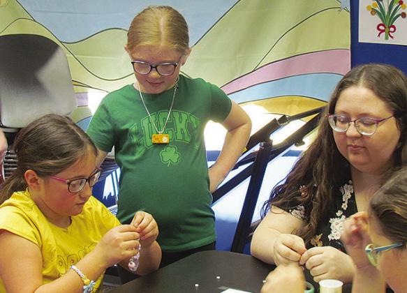 From left, Ela Thomas, Joslynn Roll, and Kat Brunelle design bracelets at a “K-Pop Demon Hunters” watch party at the Clinton Public Library. CDN | Christian Jacobsen