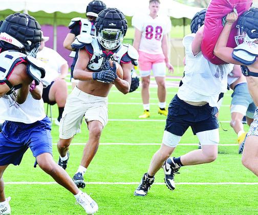 Clinton’s Jesus Gutierrez carries the ball between two blocks set by CJ Begay on DJ Lister, left, and Zaryk Baker on Vince Jones during preseason practice at the Tornado Bowl. CDN | Sam Goodwyn