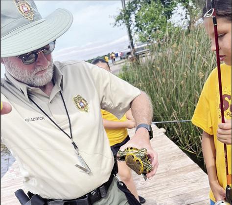Dist. 7 Chief Game Warden Je_ Headrick, left, helps Paris Nava get a turtle o_ her fishing line while on a field trip to Crowder Lake with Summer Playground. CDN | Courtesy photo