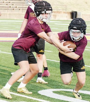 Clinton’s Liam Lofland, left, hands the ball to Dyson Moss during a drill in practice Monday night in the Tornado Bowl. CDN | Sam Goodwyn