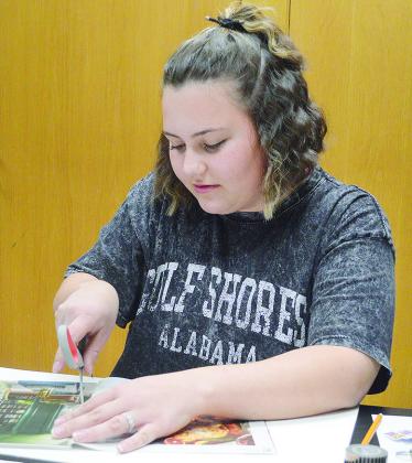 Karleigh James cuts out scraps from an old magazine to put on her 2026 vision board during an activity Monday evening at the Clinton Public Library. CDN | Micah Ashcraft