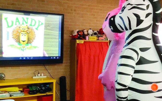 Who is that? Why, the “Masked Readers” of course. In this instance the pink axolotl is Clinton Police SRO Andrew Wilson and the zebra is SRO Dillon Whitten. The two officers were filmed reading a book for students to watch and guess the identity of th