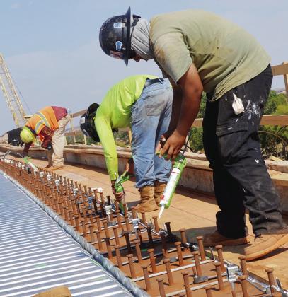 From left, Hypy Flores, Misa Gonzalez, and Eric Atilano add sealant between the pieces of metal at the construction above Neptune Drive. CDN | Christian Jacobsen