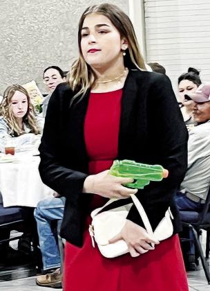 Mock trial member Kinsley Bridges, playing the role of Miss Scarlett in an adapted version of “Clue,” shows her “murder weapon” Monday night at the Frisco Center. CDN | Michael Maresh