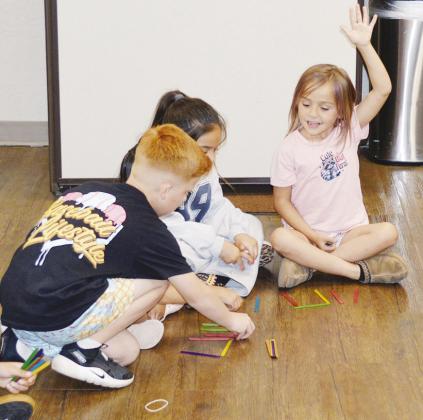From left, Owen Stockton and Adelynn Marquez work with their popsicle sticks as Stella Oliver calls over her teacher to check her answer at the Board of Education meeting. CDN | Christian Jacobsen