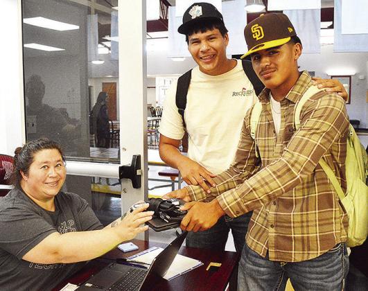 Mary Barber, left, helps Andre Lime and Jesus Gutierrez collect their Chromebooks and chargers to use for the rest of the year during the first day of school at Clinton High School. CDN | Micah Ashcraft