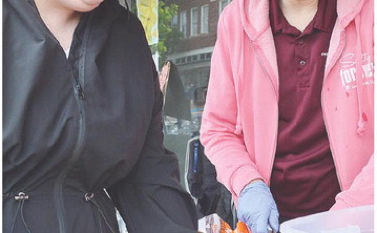 Taylor Hamlin, left, and Brenda Burton cut up orange slices Saturday morning on Frisco Avenue to hand out to runners as they finish their races during the Clinton Classic Run. CDN | Micah Ashcraft