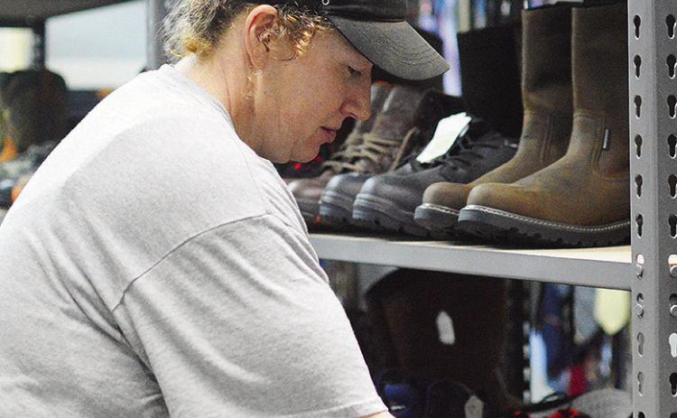 Mickie Haag stocks several pairs of newly donated boots to the “Boot Room” shelves Wednesday morning at the Clinton Mission House Wear It Again store. CDN | Micah Ashcraft