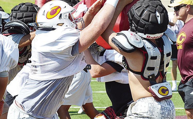 Clinton’s Brayden Fuller, left, pushes through the blocking pad held up by teammate Dyson Moss during practice in the Tornado Bowl. CDN | Sam Goodwyn