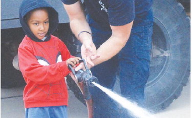 Ezra James, left, carefully pulls the lever with Lt. Billy Gerstenkorn and shoots traffic cones during the Cheyenne and Arapaho Head Start field trip at the Clinton Fire Department. CDN | Christian Jacobsen