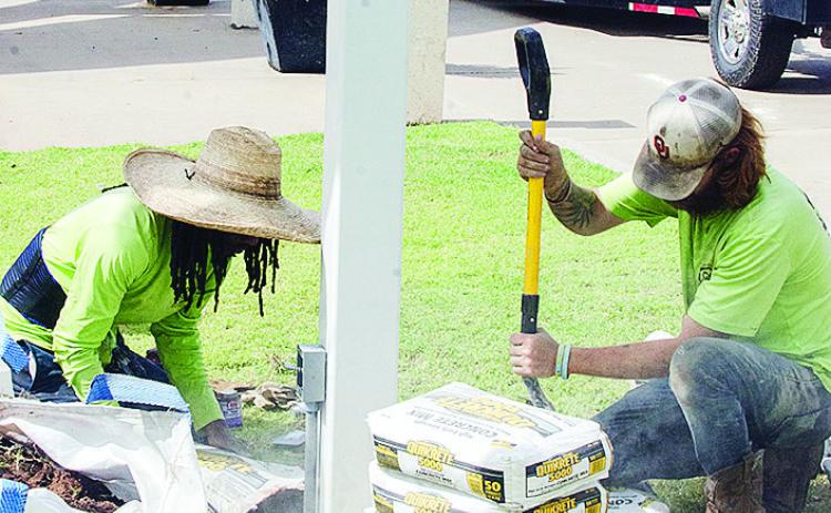 Cameron Jones, left, and Caleb Mabry work on cementing the pole in place Thursday that will hold a new Route 66 centennial sign outside of the Frisco Center. It’s visible on the trailer in the background. CDN | Sam Goodwyn