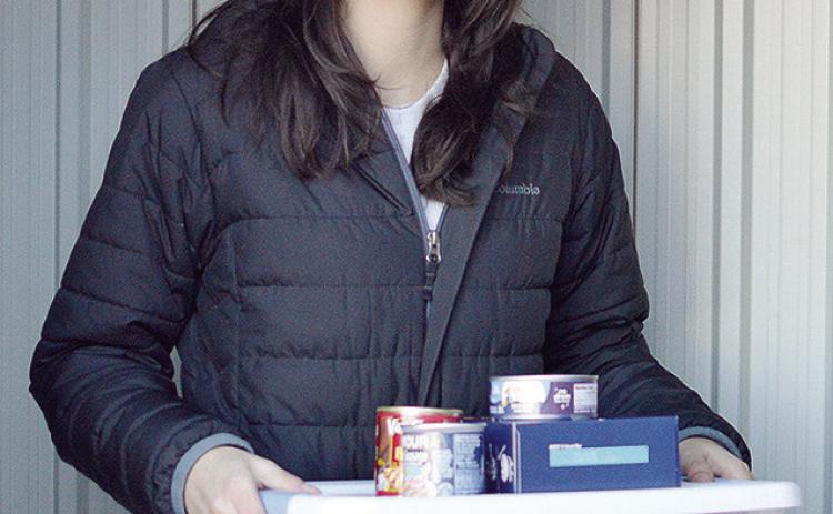 Carys Garcia carries a stack of donated food to the community food box she set up behind the Garcia Law offices Wednesday morning. CDN | Micah Ashcraft