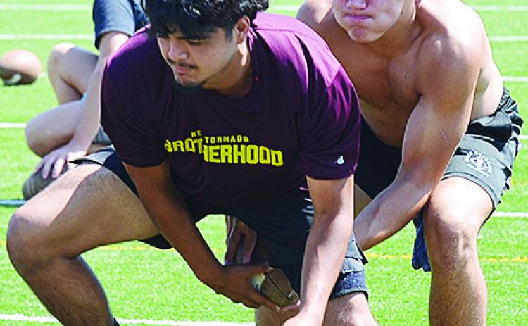 Clinton’s Aaron Ramirez, left, hikes the ball to sophomore quarterback Easten Powell during practice in the Tornado Bowl. CDN | Sam Goodwyn
