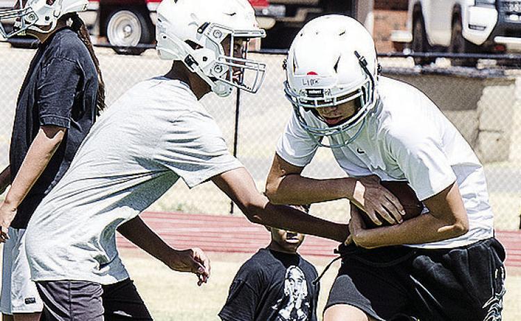 Zaithan Whiteshirt, left, hands the ball off to Camron Lime during the first day of middle school football practice at the high school practice field. CDN | Sam Goodwyn