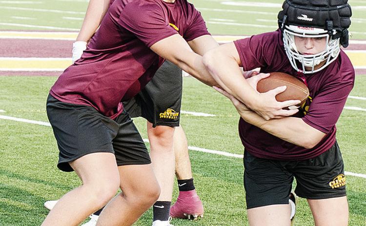 Clinton’s Liam Lofland, left, hands the ball to Dyson Moss during a drill in practice Monday night in the Tornado Bowl. CDN | Sam Goodwyn